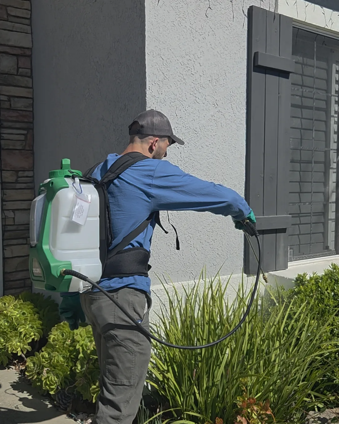 Technician treating a planting bed against the side of a house