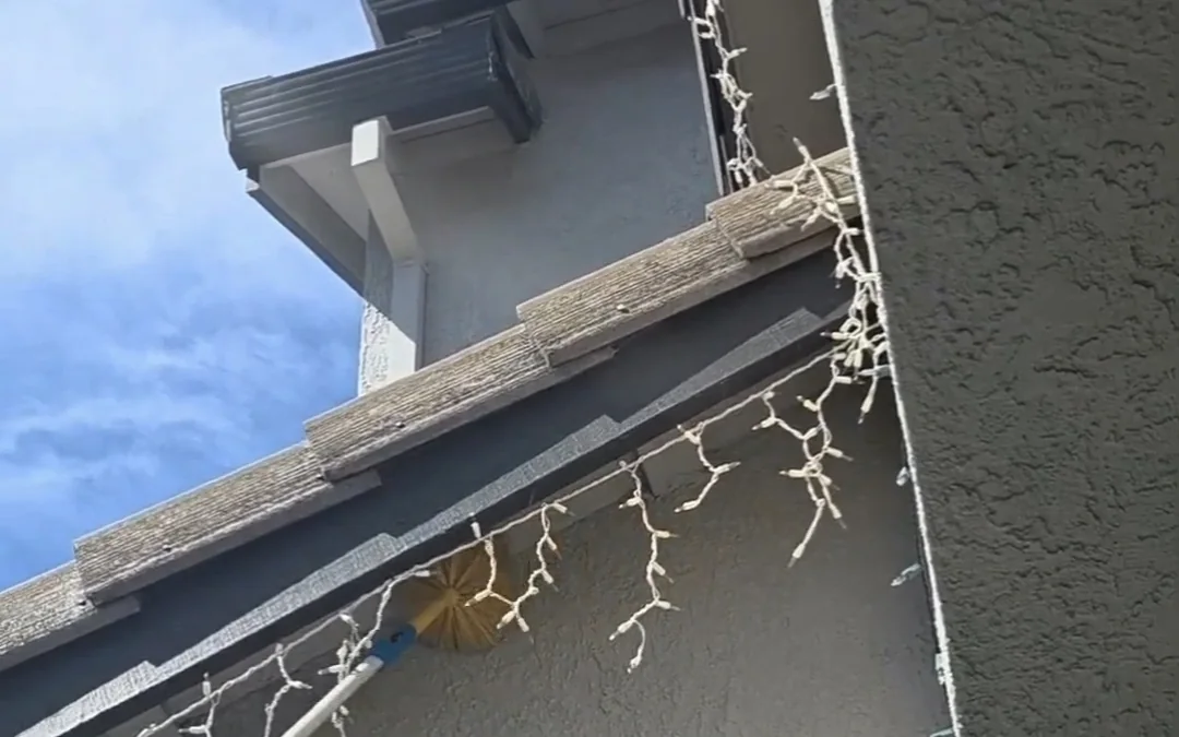 Roofline and eave of a two-storey home being cleared of spider webbing with an extension pole