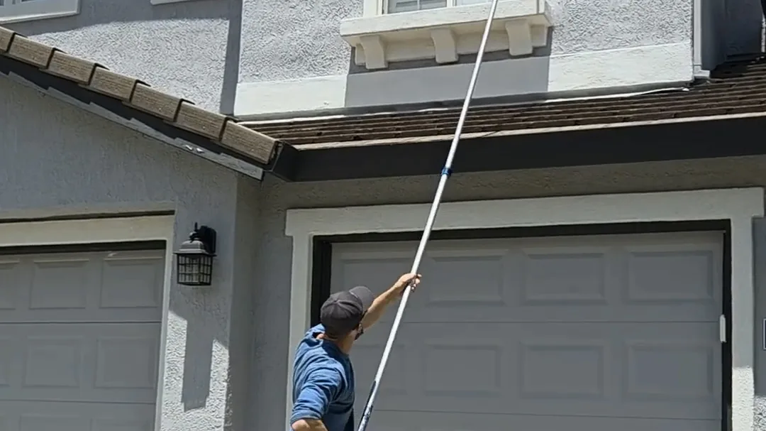 Technician clearing webbing from garage eaves with an extension pole