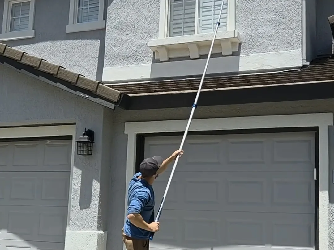 Technician clearing webbing from garage eaves with an extension pole