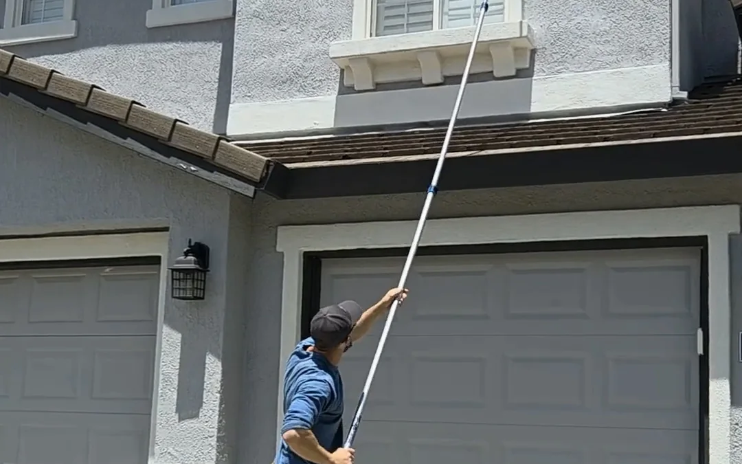 Summit Pest Control technician clearing webbing from garage eaves with an extension pole